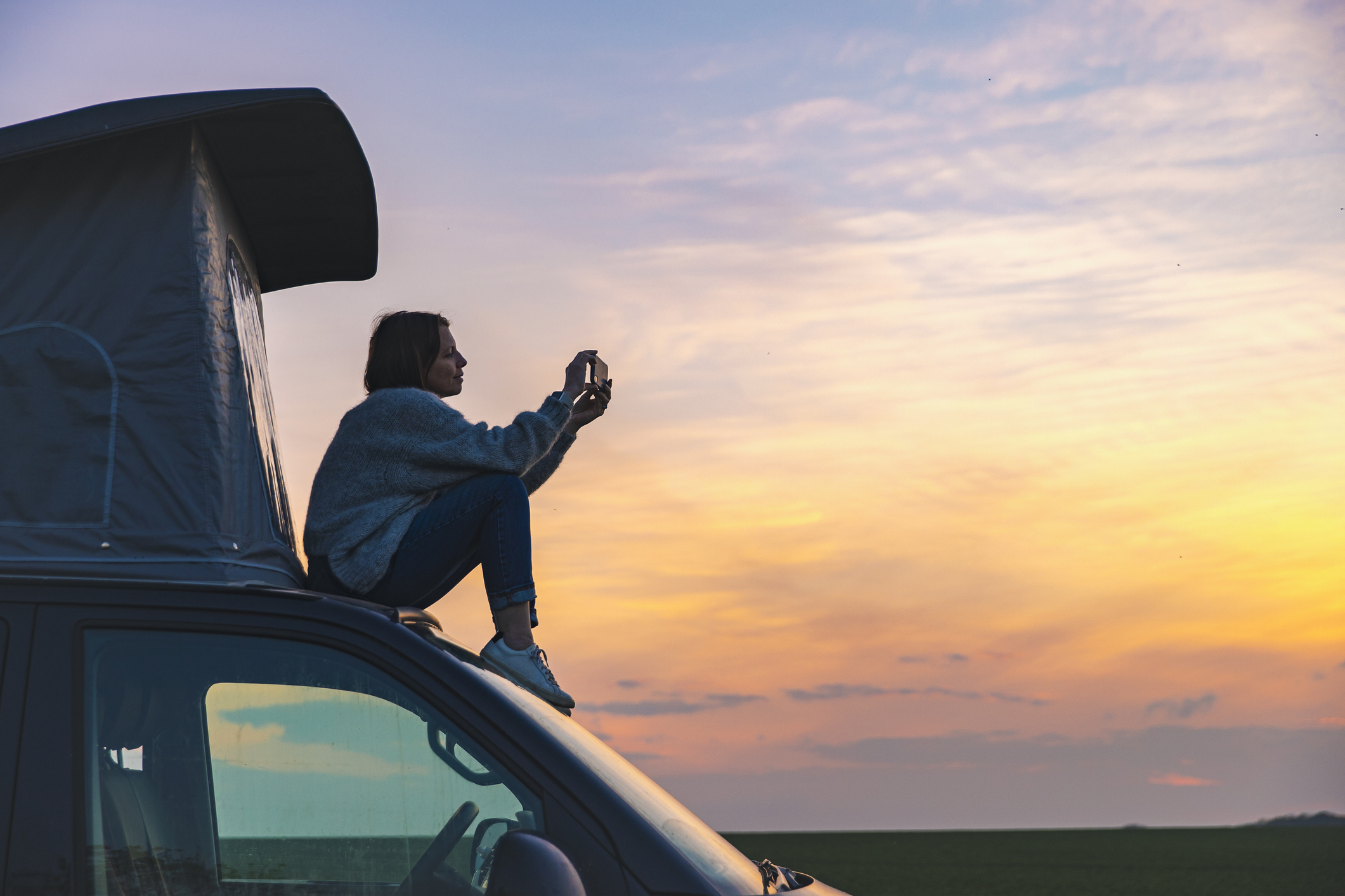 Woman photographing the sunset from the rood of her campervan