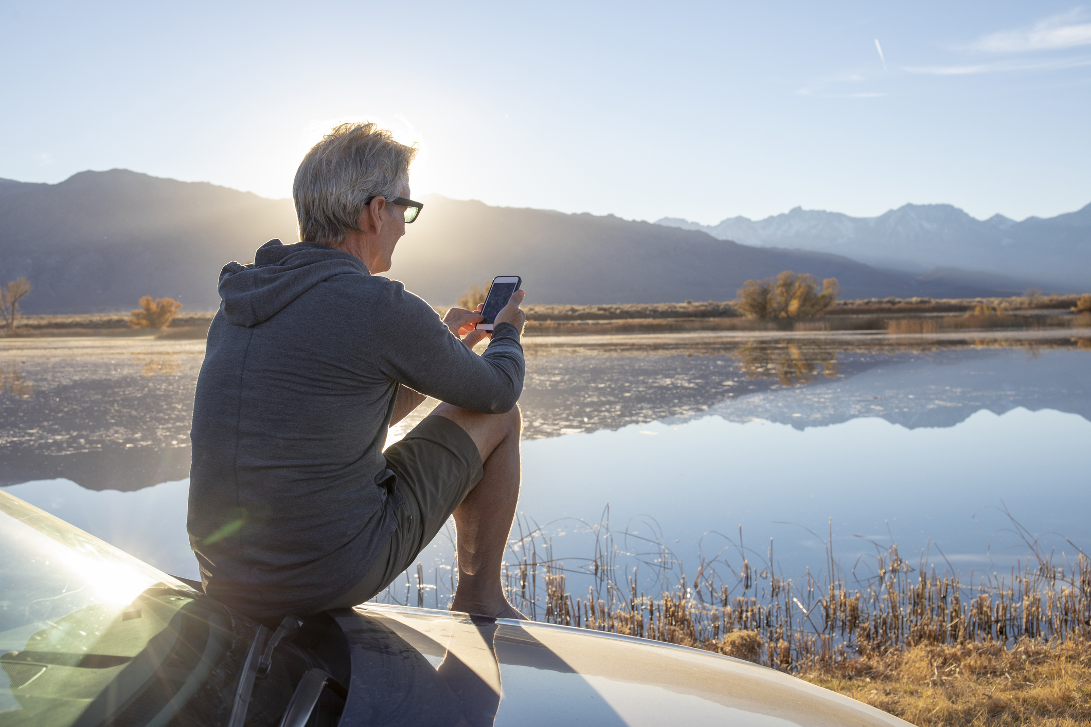 Man relaxes on car hood, looks out to sunrise