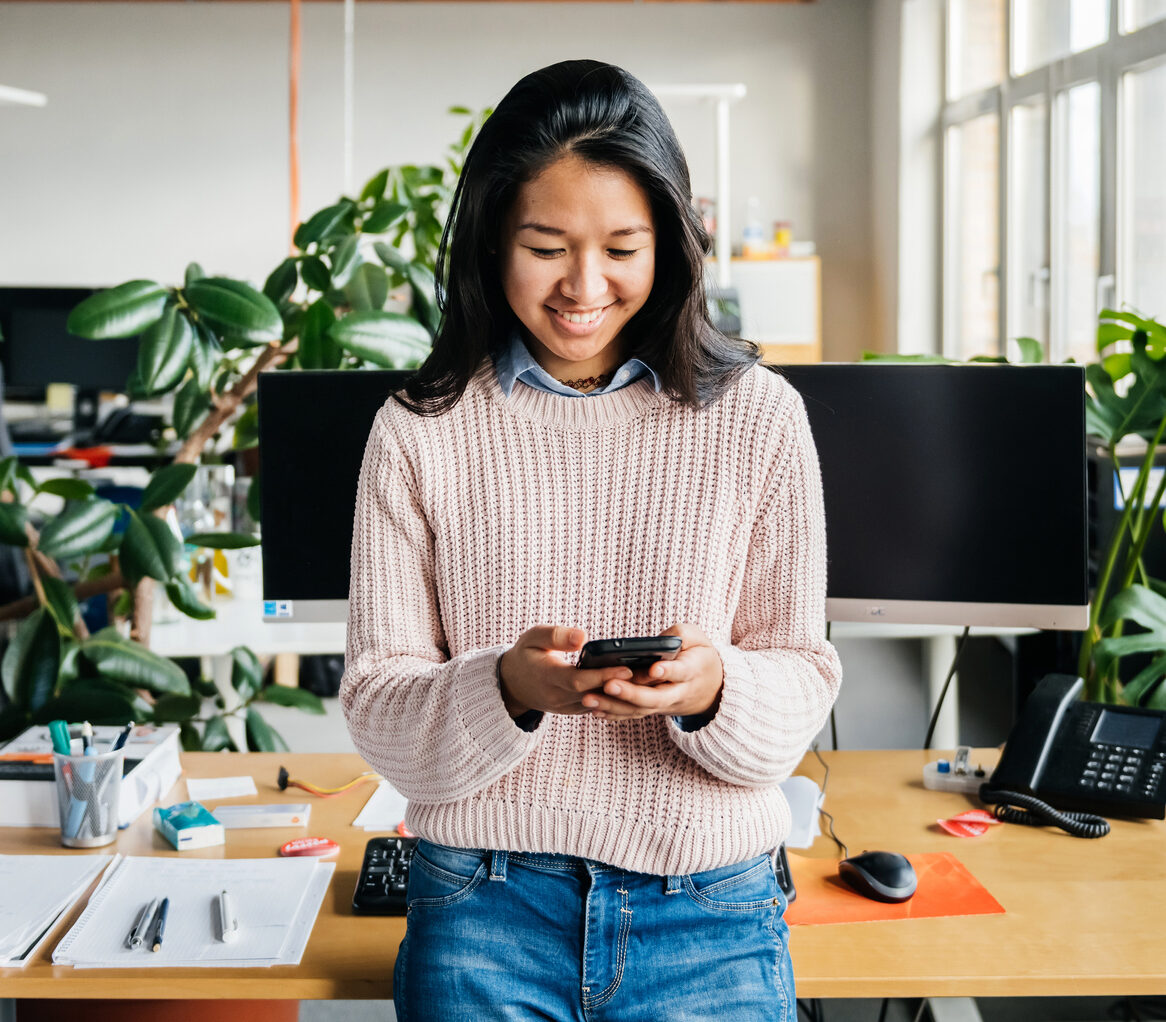 Young Office Employee Using Smartphone At Desk